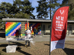 A table of paint pots, beside a group of adults and children painting a wall in a park with bright colours. The Volunteering Canterbury banner in the foreground