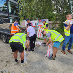 A team of people wearing hi-vis vests fill bags with sand from the back of a truck