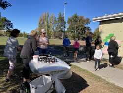 A table of paint pots, beside a group of adults and children painting a wall in a park with bright colours