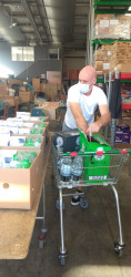 A man wearing a face mask stands with a trolley full of drinks, at a long table covered in boxes