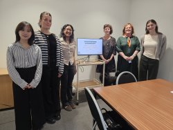 Six individuals stand around a screen displaying a presentation that reads "Volunteering Canterbury: 2026 United Nations International Volunteer Year