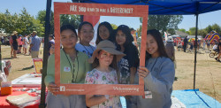 Five high school student volunteers and a child stand in front of a blue gazebo and look through the red cardboard sign that reads "Are you ready to make a difference?