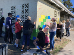 A group of adults and children painting a wall in a park with bright colours