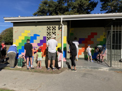 A group of adults and children painting a wall in a park with bright colours