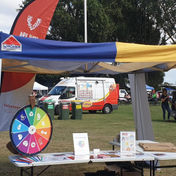 The Volunteering Canterbury stand set up at Culture Galore with a flag, the Wheel of Opportunity, and various posters and brochures on a table
