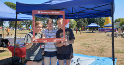 Three high school student volunteers stand in front of a blue gazebo holding a red cardboard frame that reads "Are you ready to make a difference?