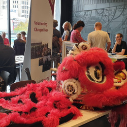 A large, fluffy Chinese Dragon displayed on a table. The Volunteering Canterbury banner in the background