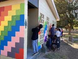 A group of adults and children painting a wall in a park with bright colours