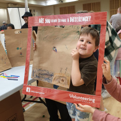 A young boy looking through the red Volunteering Canterbury frame, holding a decorated brown paper bag