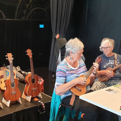 Two women sitting at a table playing ukeleles