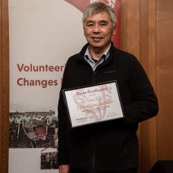 Simon Loi with his Award, in front of the Volunteering Canterbury banner