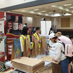 The Volunteering Canterbury stand at CultureFest Selwyn, 2023. Two large banners, behind a table of brown paper bags & coloured pens, and volunteer students in high-vis vests