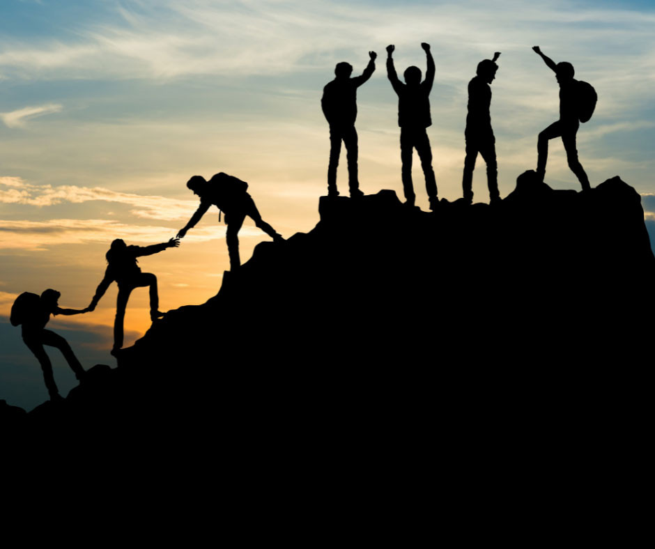 Silhouettes of people helping each other to climb the peak of a hill