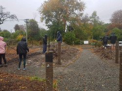 Two teams of people in the rain, using large sticks to create screening frames in a community garden