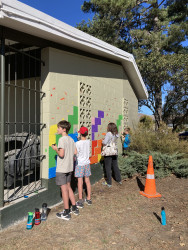 A group of adults and children painting a wall in a park with bright colours