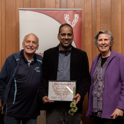 Sanjeewa Thanushka and two supporters, with his Award, in front of the Volunteering Canterbury banner