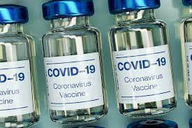 Small glass bottles with blue lids. Bottle labels read "Covid-19. Coronavirus Vaccine"