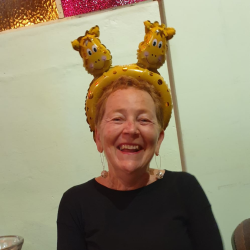 VolCan staff member, Alison, with a broad smile, while wearing an inflatable headpiece with two giraffe faces on it