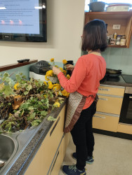 A women in an apron in a commercial kitchen, preparing herbs