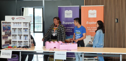 A display table for Canterbury Masters Figure Skating Club on the left. On the right, three people stand behind a display  table for Imagination Station