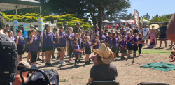 A group of young people wearing purple shirts, performing in front of a crowd