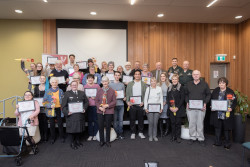 The group of Award recipients, standing at and in front of the stage, holding their awards and flowers