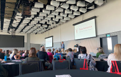 The conference room, overlooking tables of audience members, and the stage at the front