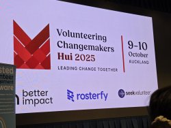 A large screen at the VNZ Hui displaying the date, Hui logo and text that reads "Volunteering Changemakers Hui 2025 Leading Change Together"