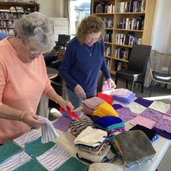 Two women lay out peggy squares, ready to be sewn together into blankets