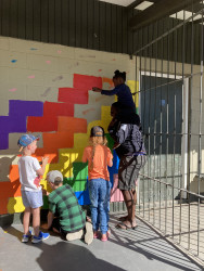 A group of children and an adult painting a wall in a park with bright colours