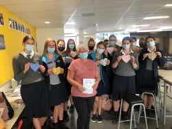 A large group of people stand together holding up sewn fabric hearts