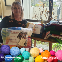 A staff member from Ranui House with a pile of Knit for Purpose blankets