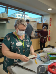 A woman in a commercial kitchen, preparing food. Two other people in the background