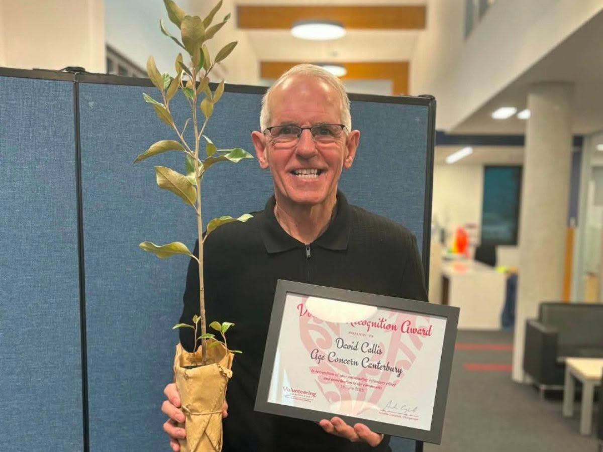 Volunteer at Age Concern Canterbury, David, smiles towards the camera, holding a seedling and his Volunteer Recognition Award.