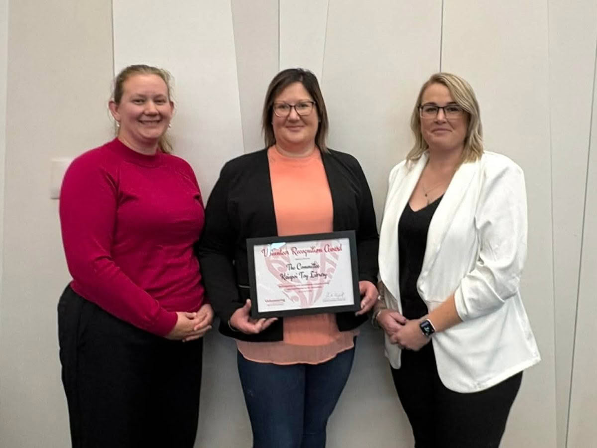Three women, from the Kaiapoi Toy Library, stand together smiling for the camera, holding their 2026 Volunteer Recognition Award.