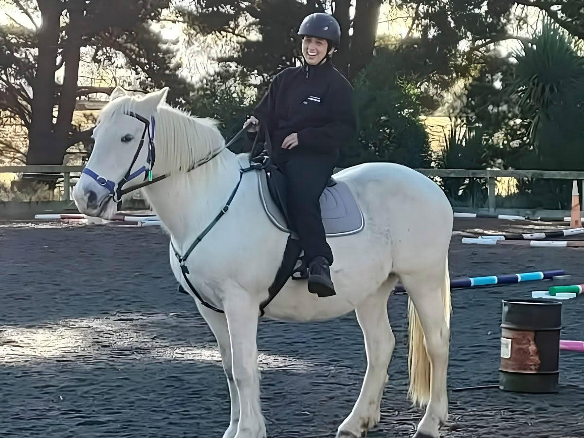 A young women sits upon a white horse, smiling broadly.