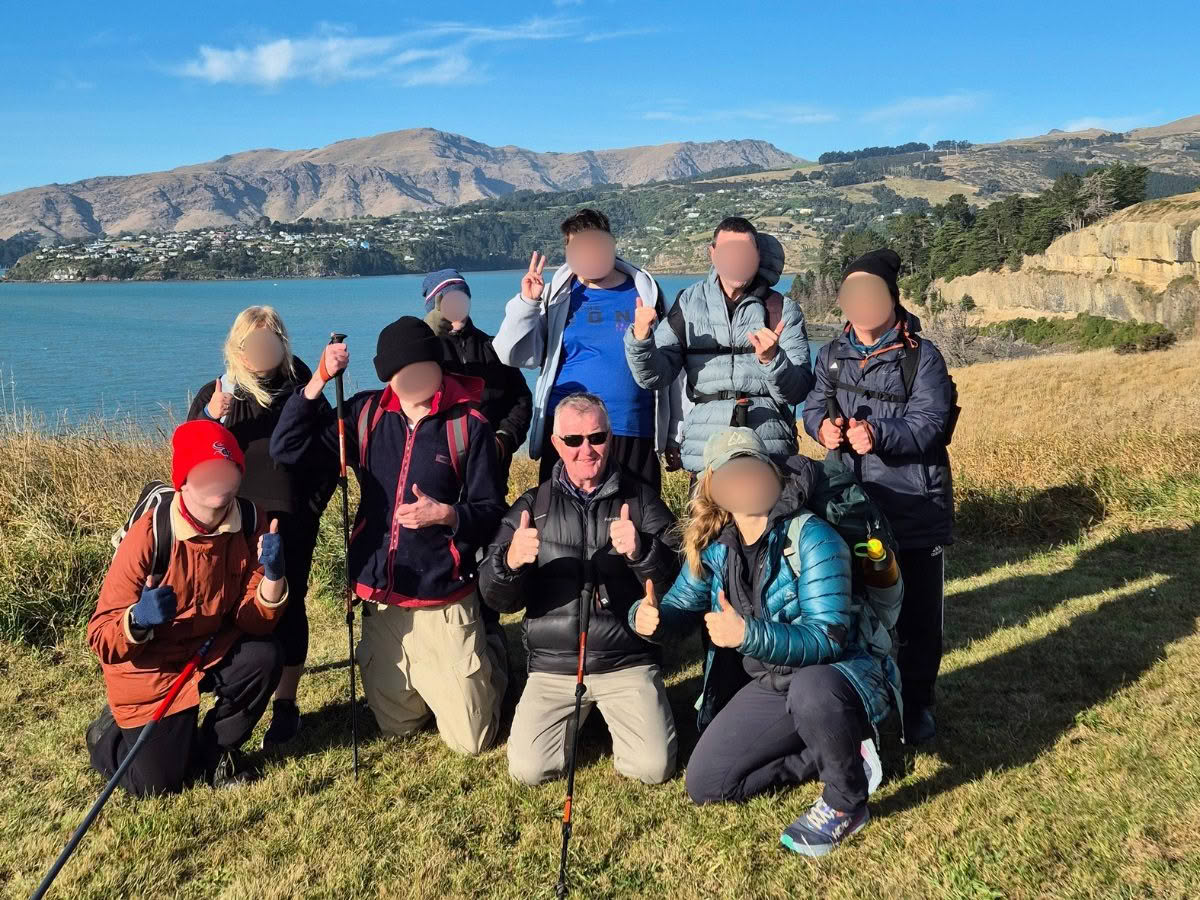 A group of hikers stand together at the top of a hill, showing thumbs up to the camera.