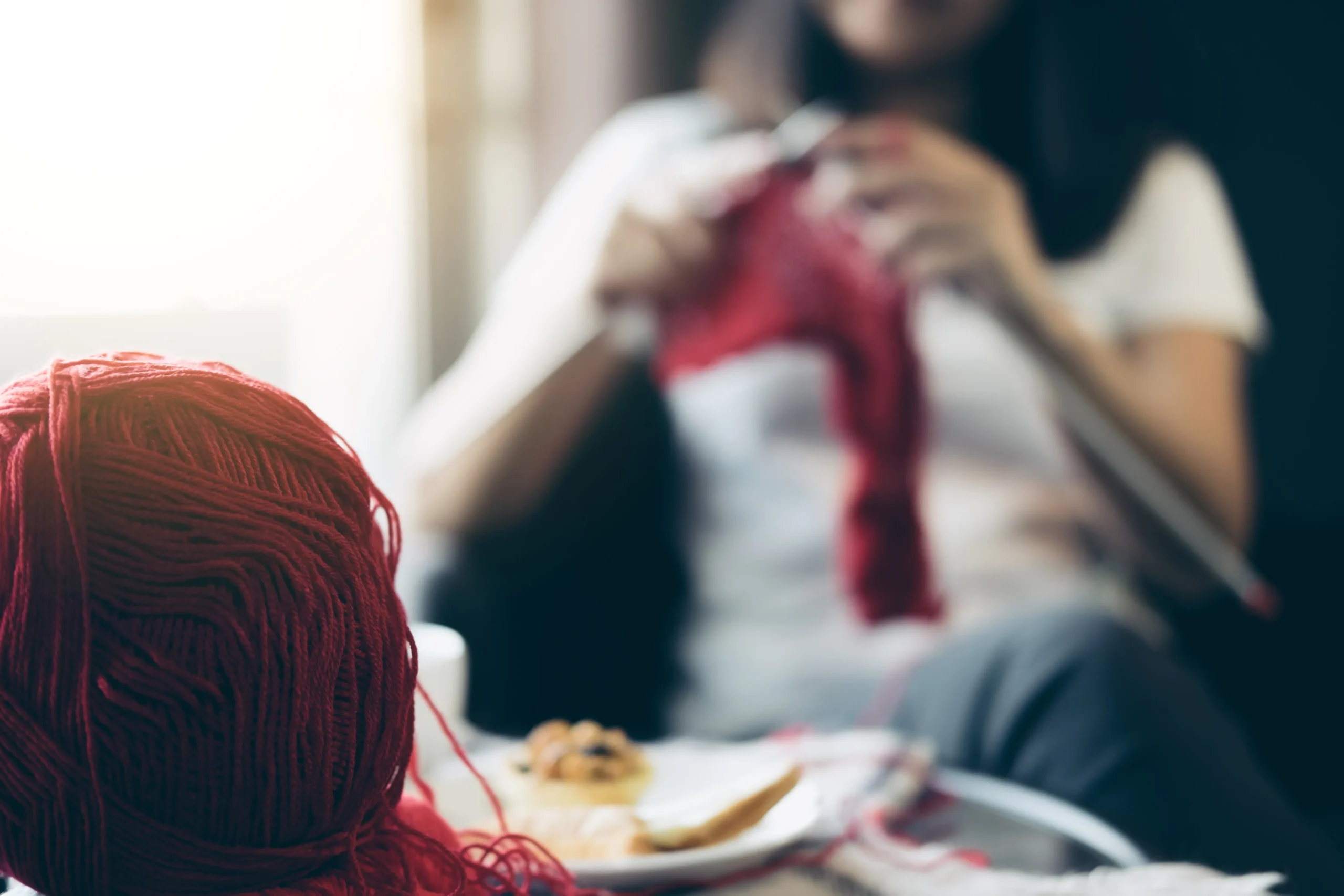 Close up shot of young woman's hands knitting a red scarf